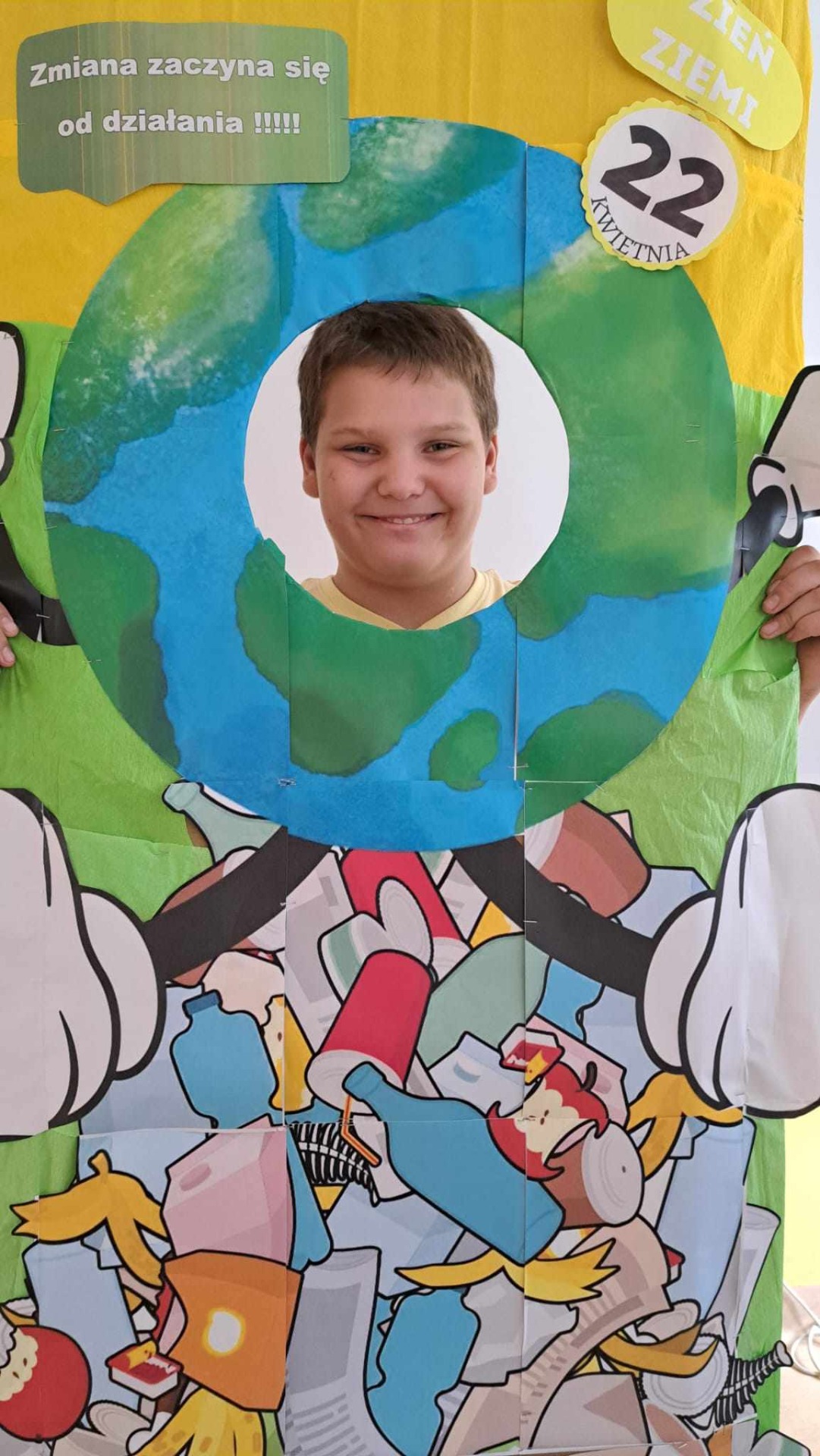 Uśmiechnięty chłopiec w ekologicznej foto-budce. Osią fotobudki jest planeta ziemia (w której jest głowa )