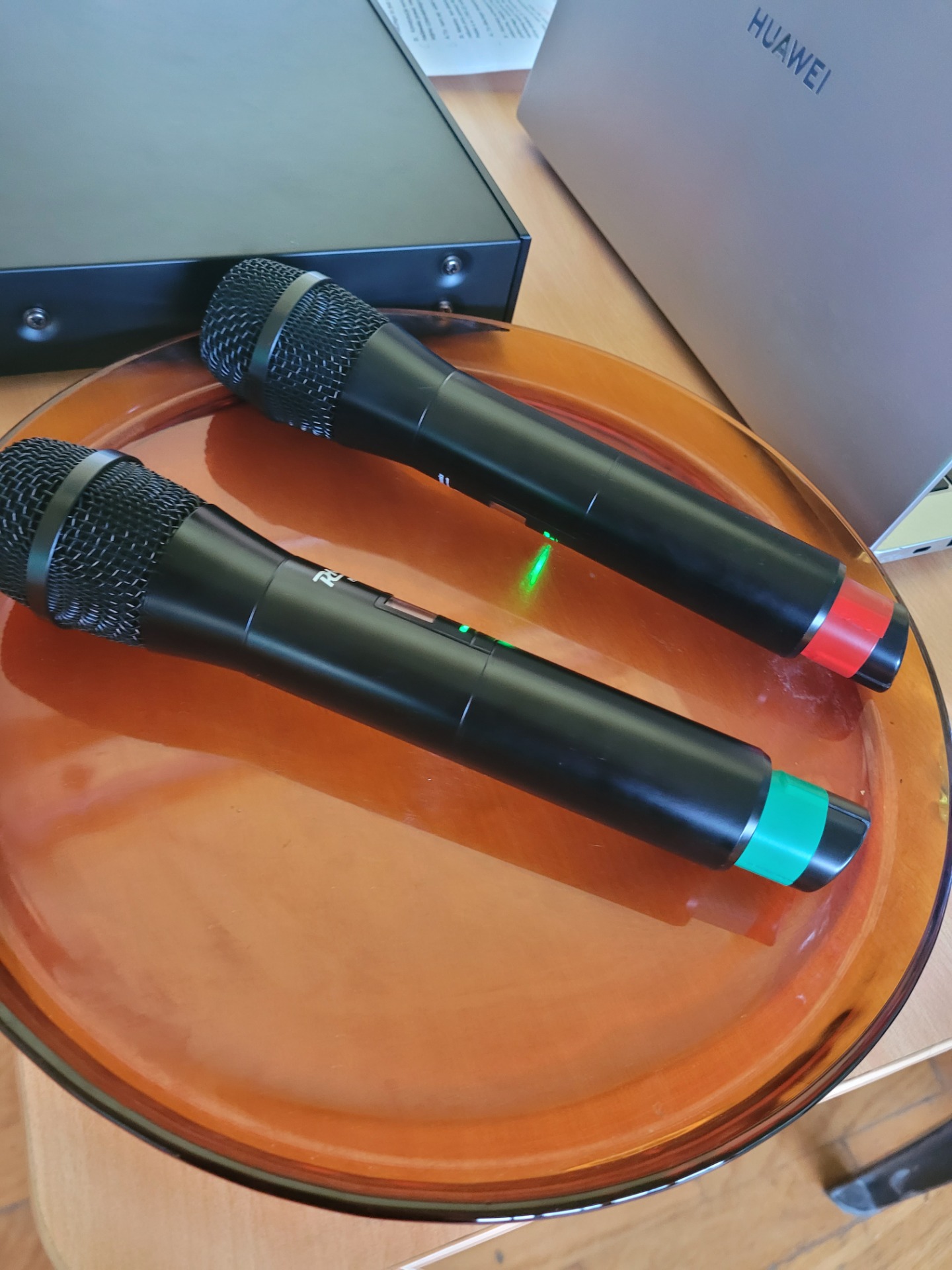 Dwa mikrofony leżą na pomarańczowej szklanej podstawce.