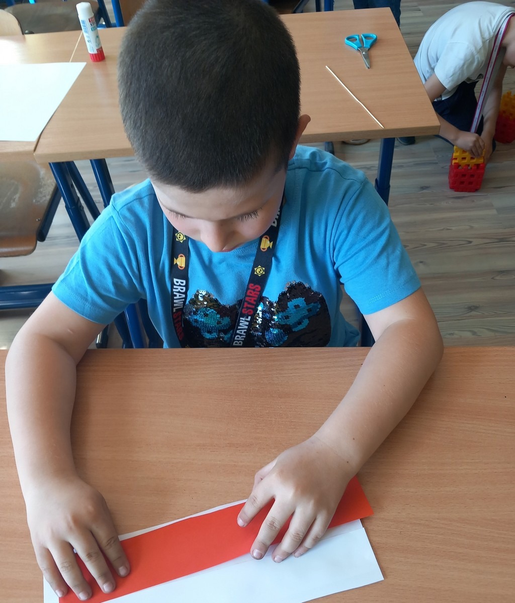 Uczeń przykleja czerwony papier do białego.