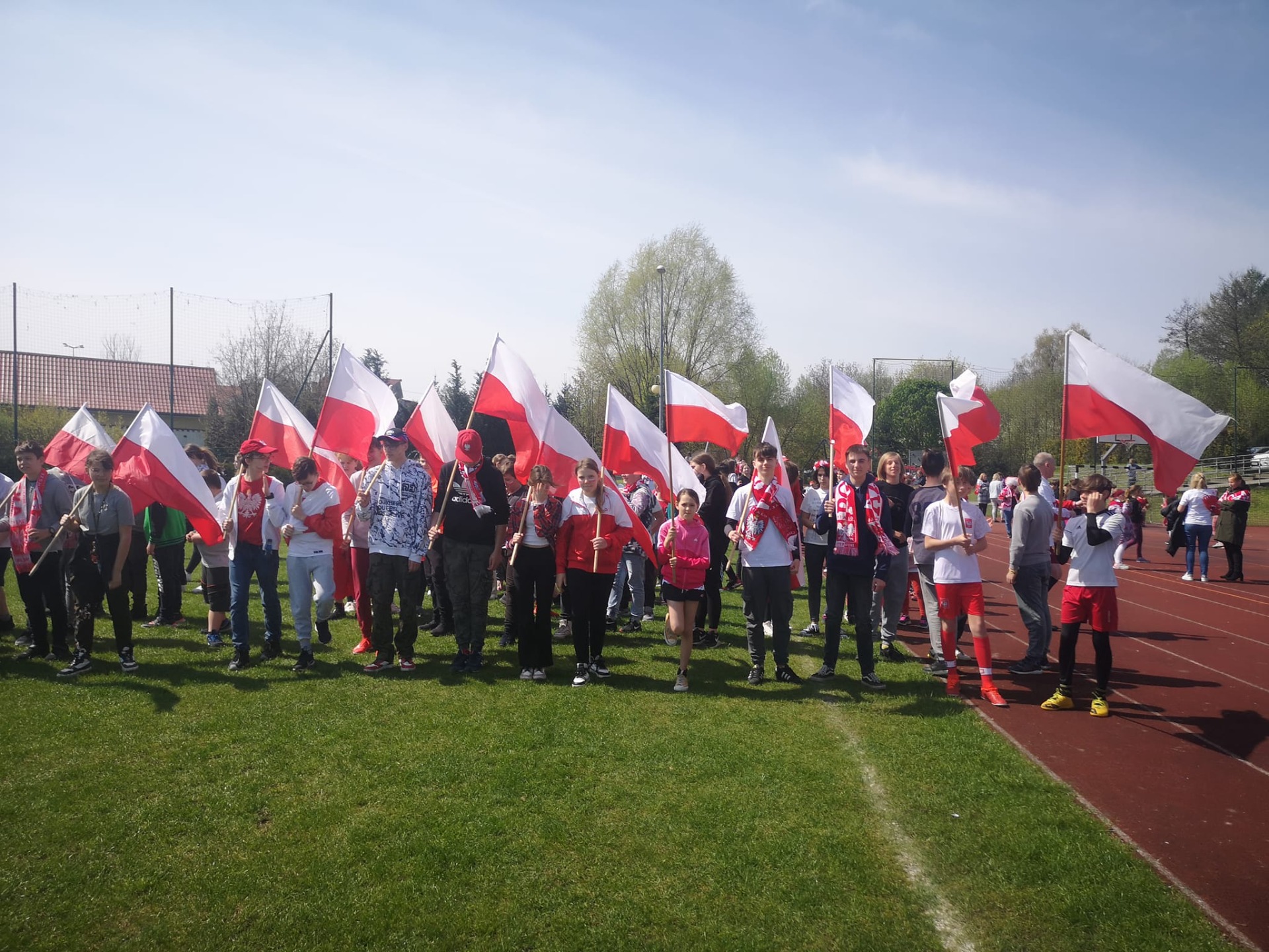 Grupa ludzi w biało-czerwonych strojach na boisku szkolnym