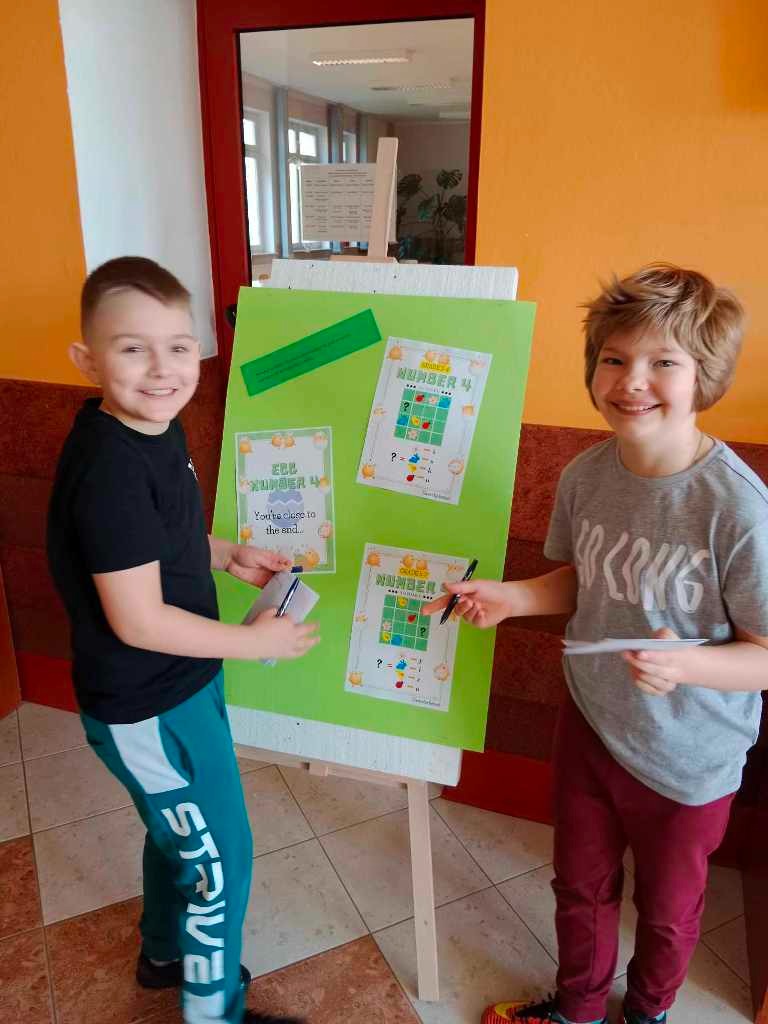 Zdjęcie przedstawia dwóch chłopców stojących przy tablicy z zadaniami konkursowymi – łamigłówkami sudoku
