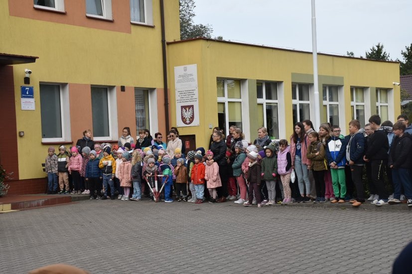 Uczniowie i nauczyciele na placu przed budynkiem szkoły na uroczystym poranku z okazji 17. rocznicy nadania Szkole imienia