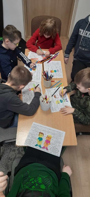 grupa dzieci siedzi przy stoliku i koloruje kolorowanki