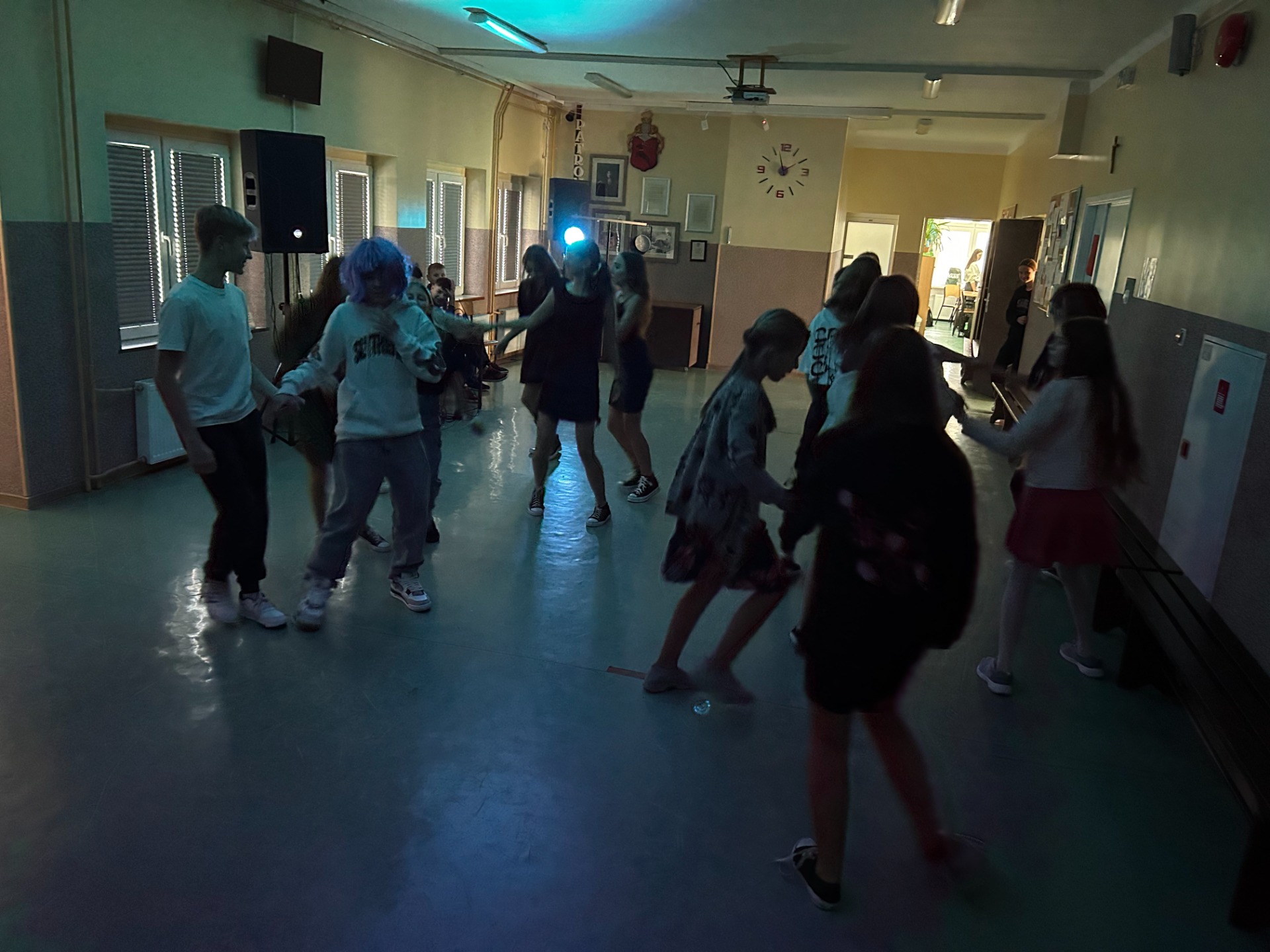 Grupa uczniów, chłopców i dziewczynek tańcząca na szkolnym holu podczas zabawy Andrzejkowej. 