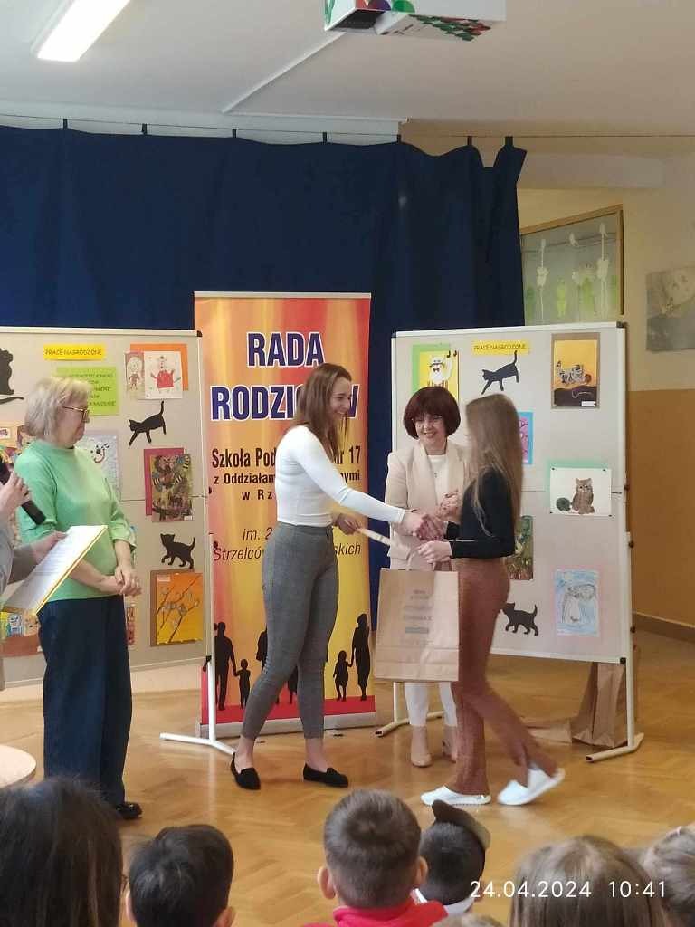 Zdjęcie przedstawia uczennicę odbierającą od Jury nagrodę w XIV Wojewódzkim Konkursie Plastycznym "Rysowane wierszyki".