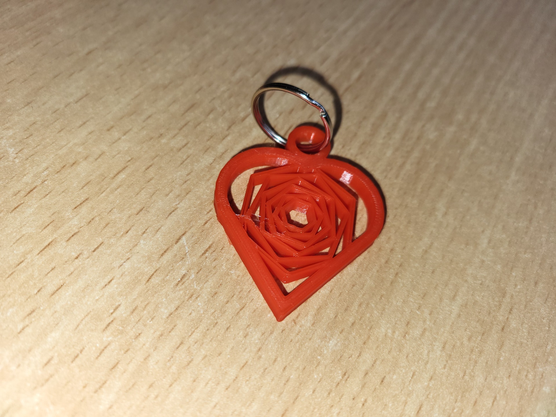 Czerwony breloczek w kształcie serca wykonany na drukarce 3D na srebrnym kółeczku do kluczy.