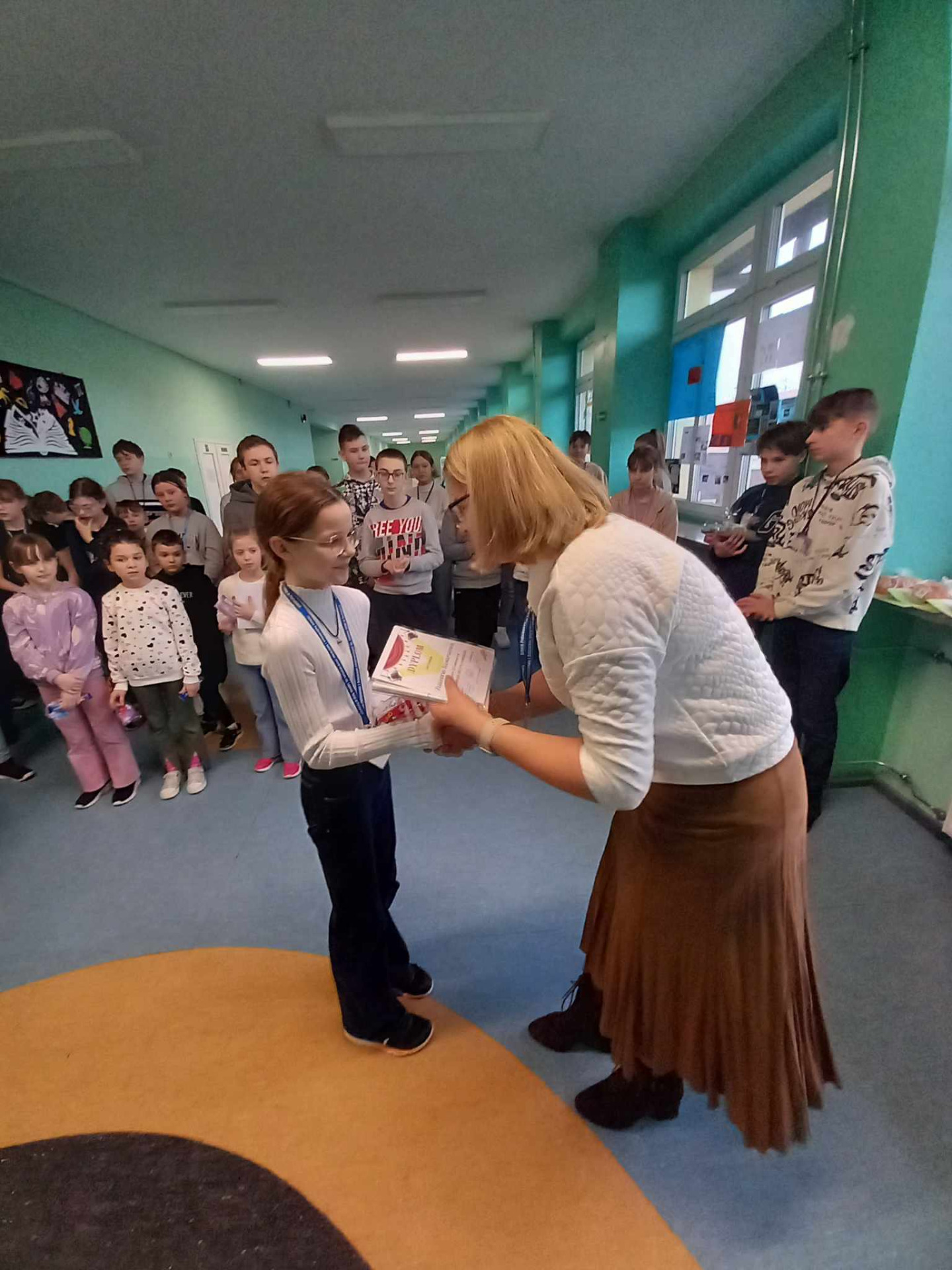 Pani wicedyrektor Lucyna Kopciewicz wręcza nagrodę uczestnikowi konkursu podczas podsumowania Dni Kultury Języka Polskiego. W tle pozostali uczestnicy.