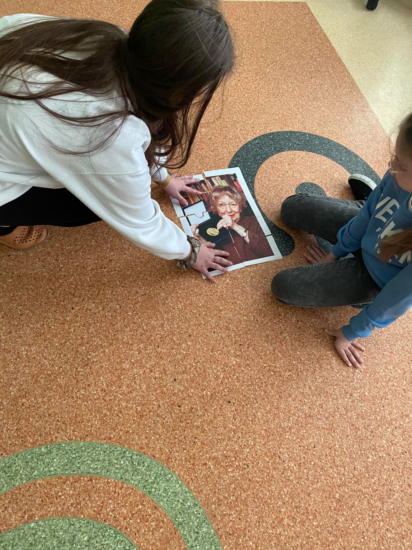 Dwie dziewczynki układają na podłodze puzzle z wizerunkiem Wisławy Szymborskiej 