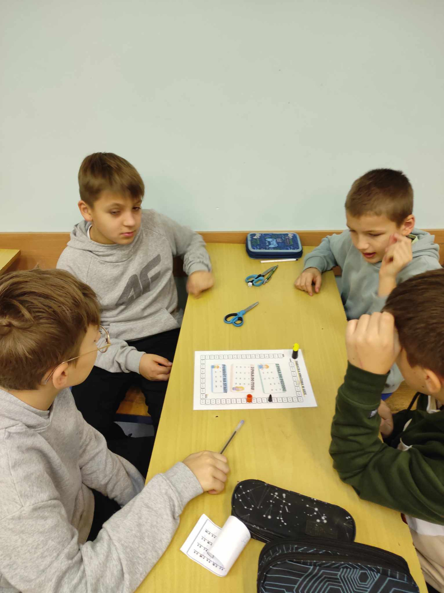 4 uczniów siedzi przy stoliku i gra w planszówkę - tabliczka mnożenia w grze