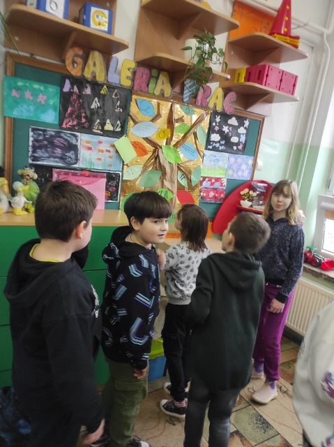 5 uczniów stoi pod tablicą ścienną, na której zamieszczone są kolorowe obrazki.